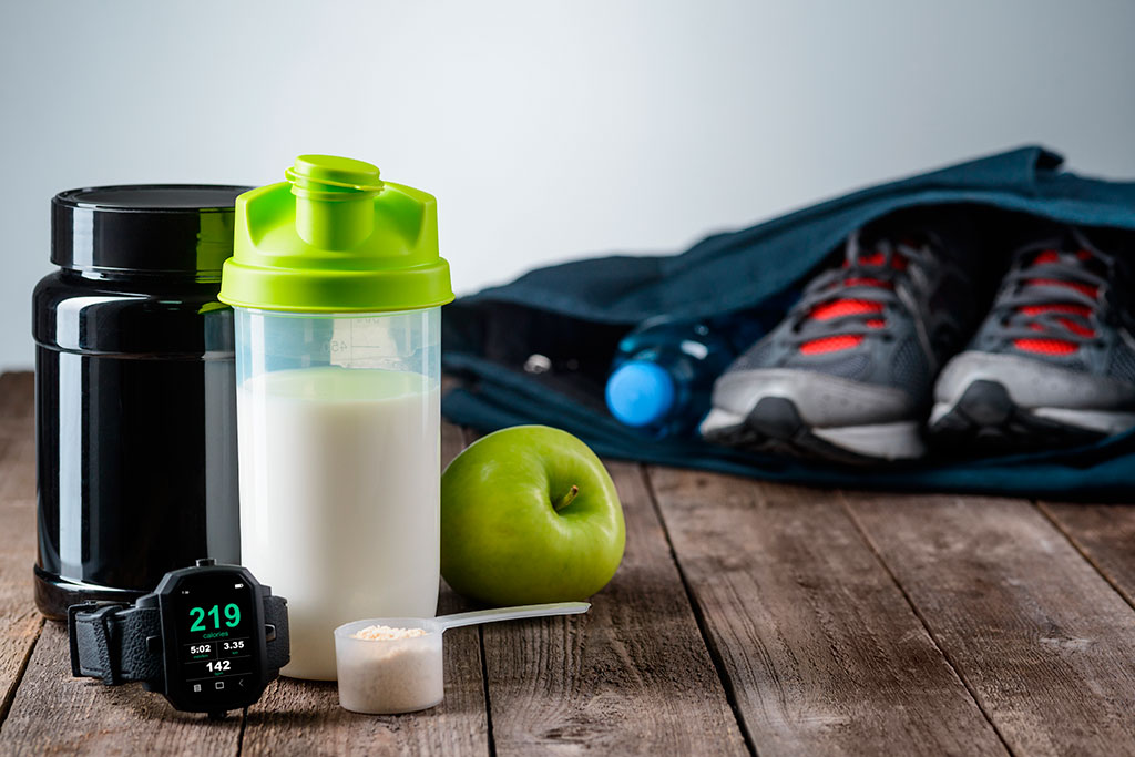 personal trainer servizio. Nella foto scarpe da ginastica, orologio, mela, acqua, bevanda isotonica e integratori alimentari