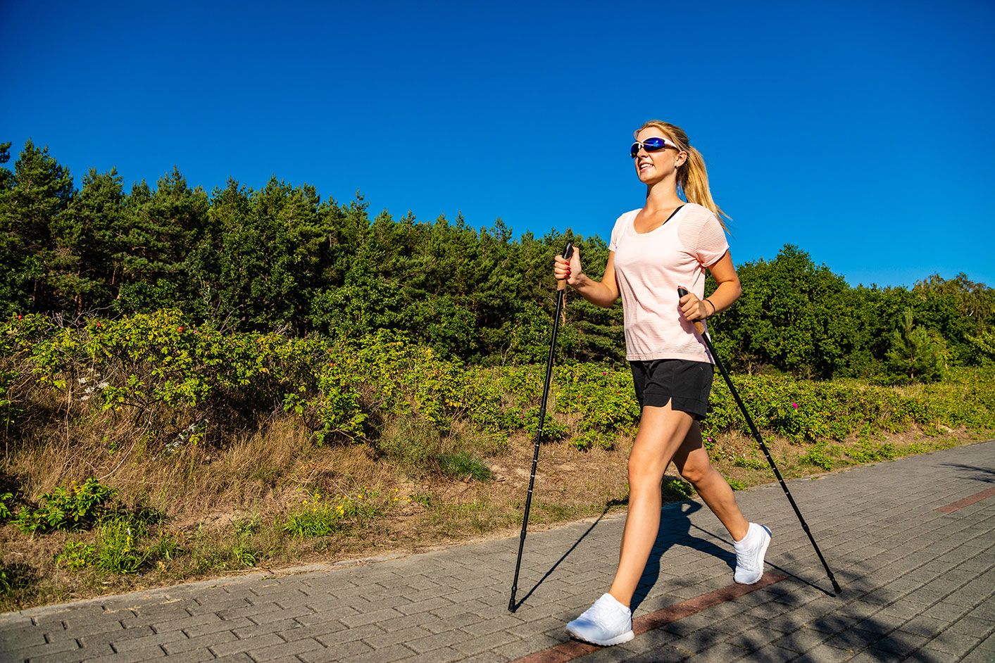dieta nordic walking, giovane donna cammina lungo il percorso ciottolato per un allenamento con bastoncini